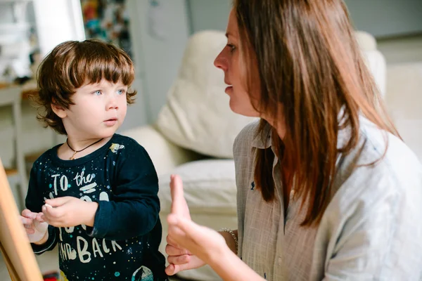 La jeune mère dessine une craie sur un tableau noir avec son jeune fils. T — Photo