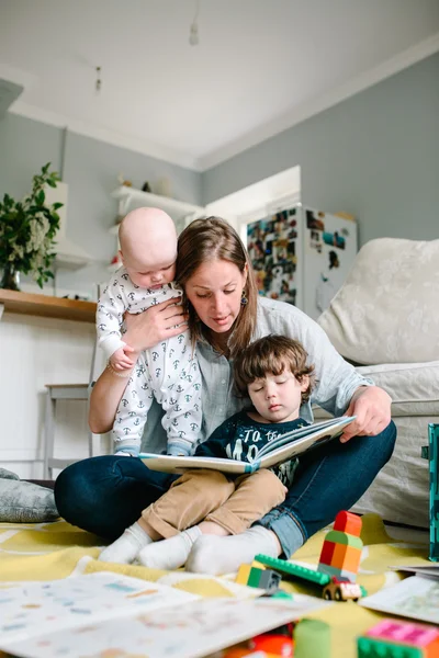 Mutlu genç anne evin zemininde oturan çocuklarına bir kitap okuyor. Aile kavramı
