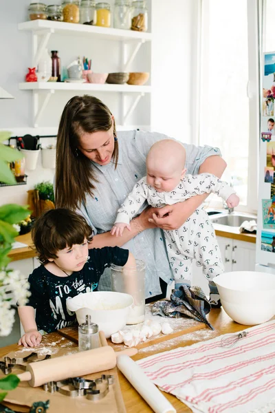 Young and happy mom with her children in the kitchen cook cookie — Stock fotografie