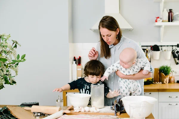 Young and happy mom with her children in the kitchen cook cookie — Stock Photo, Image