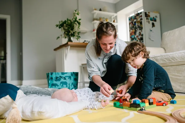 Madre joven y feliz jugando con sus hijos pequeños en el suelo de la casa. Los niños se ríen. Concepto de familia — Foto de Stock