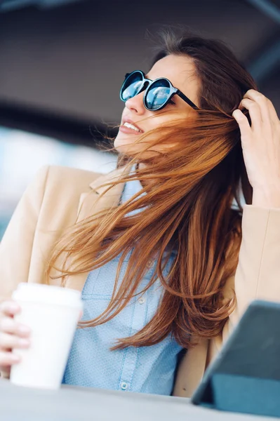 Menina bonita e jovem em óculos de sol bebendo café na rua e lendo as notícias em um tablet — Fotografia de Stock
