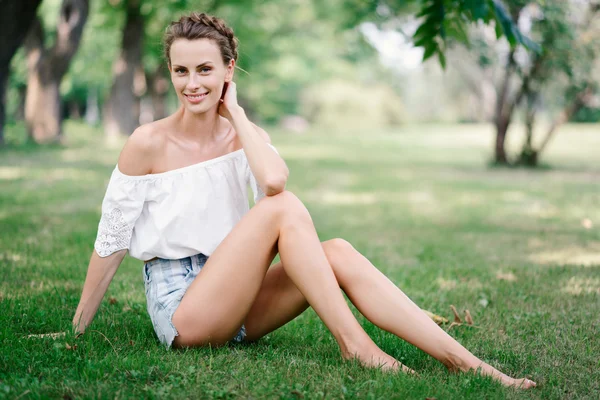 美丽性感的女孩，穿着短裤在公园的草地上休息 — 图库照片