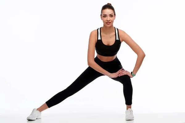 Spor giyimli güçlü fitness kadını beyaz izole edilmiş arka planda bacaklarını esnetiyor. Kadın spor eğitmeni fiziksel egzersiz yapıyor.