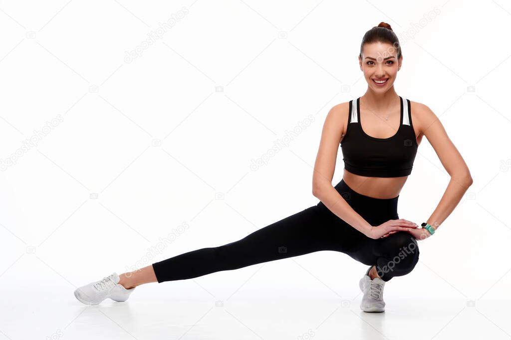 Fitness European girl doing stretching workout. Full length shot of young girl on white background. Stretching and motivation