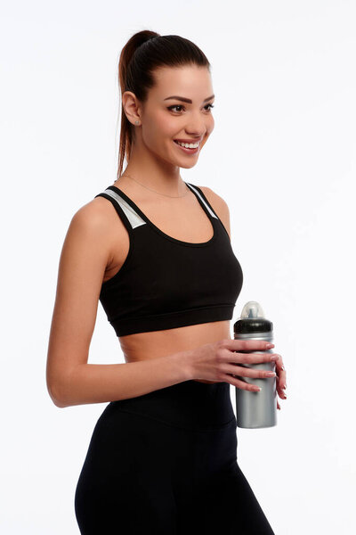 Smiling caucasian fitness instructor holding plastic bottle of water on white isolated background. Sporty woman, healthcare concept