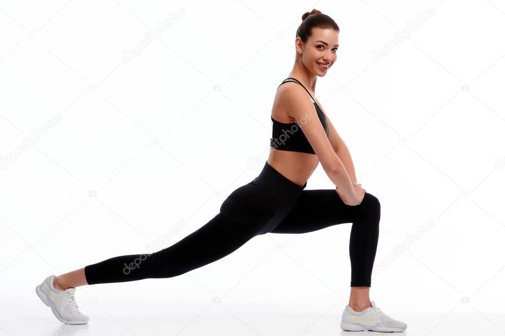 Fit strong fitness woman in sportswear stretching legs on white isolated background. Female sport instructor doing physical exercise