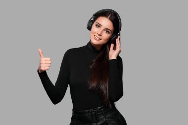 Kablosuz kulaklıklarla gülümseyen genç bir kadın baş parmak hareketini gösteriyor, bir kadın müzik dinliyor, izole edilmiş bir geçmişi var.