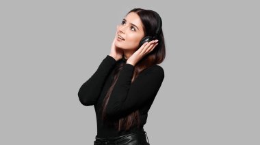 Kablosuz kulaklıklarla gülümseyen çekici kadın müzik dinler, gri arka planda izole bir şekilde.
