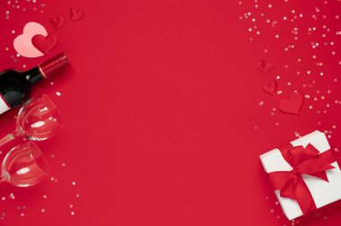 Sevgililer Günü şablonu düzdü. Şarap şişesi, bardaklar, çiçekler kırmızı arka planda hediye kutusu olan güller.