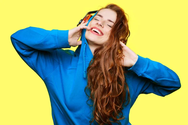 笑着穿蓝色夹克的Dj女孩听黄色背景的红色耳机里的音乐 — 图库照片