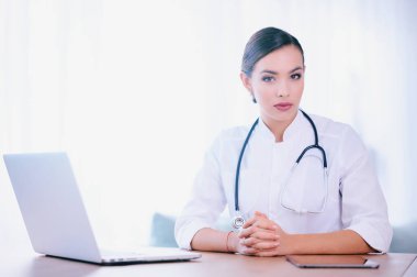 Steteskop giyen kadın doktor hastanede çalışıyor ve dizüstü bilgisayar kullanıyor.