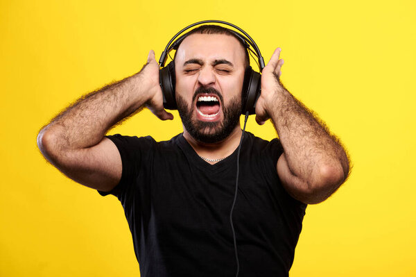 Screaming arabic man with beard listens to music with headphones on yellow isolated background. International DJ Day