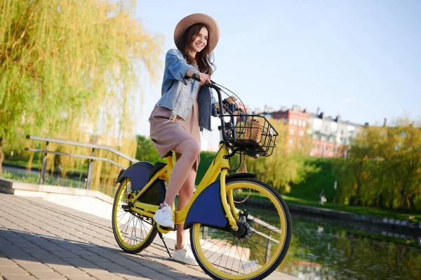 Piękna młoda uśmiechnięta kobieta w letnim stroju spaceruje po mieście i jeździ wypożyczonym rowerem nad rzeką — Zdjęcie stockowe