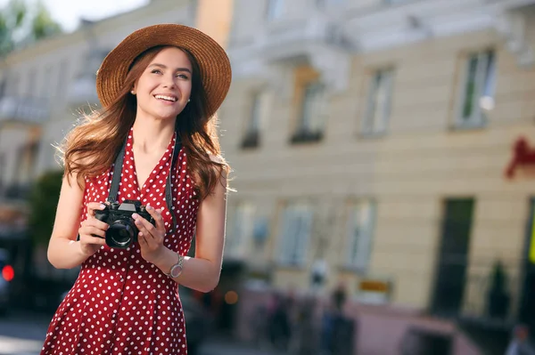Genç gülümseyen kadın turist yazın şehirde dolaşıyor ve elinde kamerayla geziyor. — Stok fotoğraf
