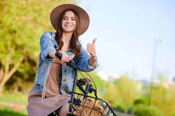 Jovem fêmea mostra polegar para cima gesto e passeios na bicicleta de aluguel ao ar livre na cidade de verão — Fotografia de Stock