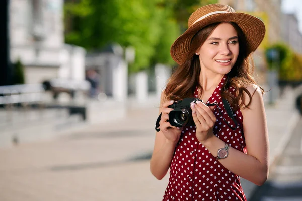 Sıradan kıyafetler giyen mutlu genç bir kadın kamerasıyla fotoğraf çeker ve yazın şehirde dolaşır. — Stok fotoğraf