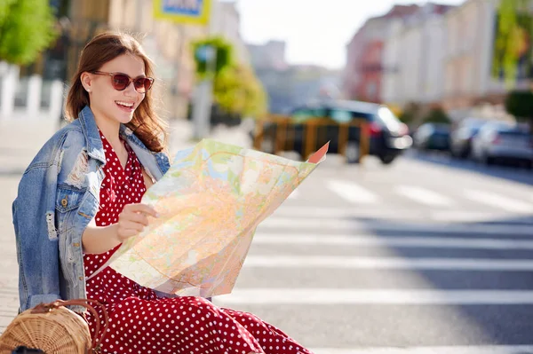 Mulher sorridente viajante sentado no chão na cidade e usa papel mapa — Fotografia de Stock