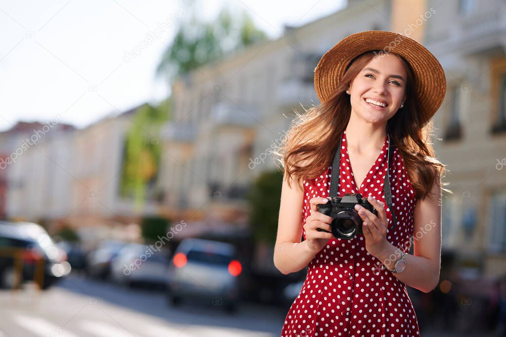 Smiling woman tourist in straw hat with camera walks in the summer city