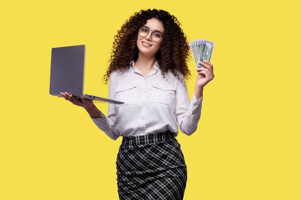 Online Casino Winner. Woman Standing With Laptop and Dollar Banknotes, enjoying money prize, happy millennial woman received e-commerce profit, standing over yellow background — Stock Photo, Image