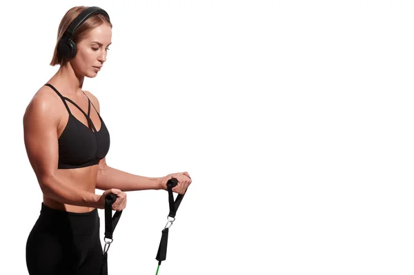 Silná svalnatá sportovkyně ve sluchátkách cvičení s odporem pás přes bílé izolované pozadí — Stock fotografie