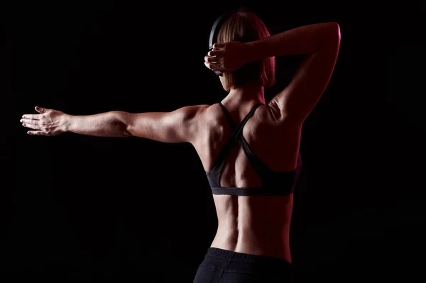 Zadní strana sportovkyně s svalnatým tělem protáhnout po cvičení. Slim dívka poslouchat hudbu při tréninku — Stock fotografie