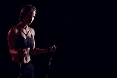 Siyah arka planda direniş bantları olan ve kulaklıkla müzik dinleyen sporcu kadın eğitimi.