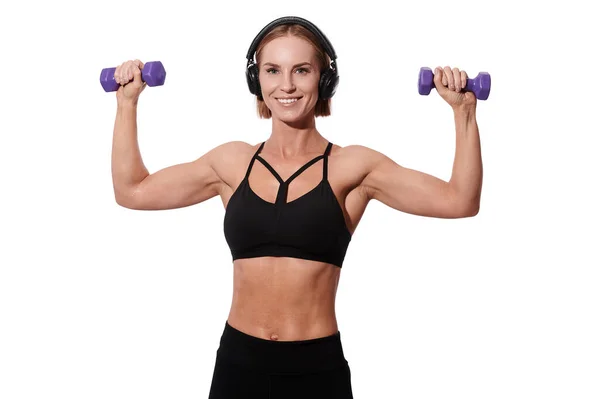 Erős izmos sportnő fejhallgató és fekete ruha csinál gyakorlat súlyzók fehér elszigetelt háttér — Stock Fotó