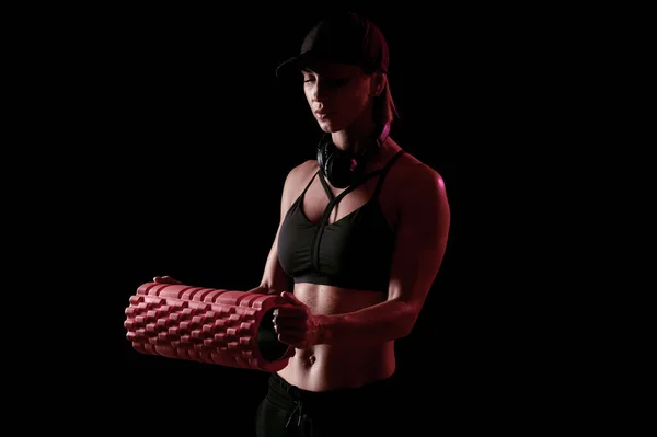 Starke athletische Frau mit Massagerolle und Kopfhörer auf schwarzem, isoliertem Hintergrund — Stockfoto