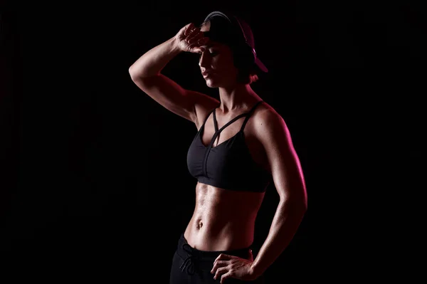 Strong woman wearing sports bra with muscular abdomen listen music in headphones over black background. Perfect Body Shape — Stock Photo, Image