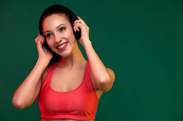 スレンダーな魅力的な笑顔スポーティな女性は仕事の後にリラックスヘッドフォンで音楽を聴く室内 — ストック写真