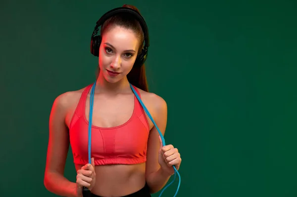 Vonzó sport nő ugrókötéllel és erős nő zenét hallgatni fülhallgatóval beltérben — Stock Fotó