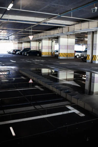 Binanın altına park etmek (otopark altı). Asfalttaki su birikintileri park yerinin duvarlarını ve tavanını yansıtıyor..