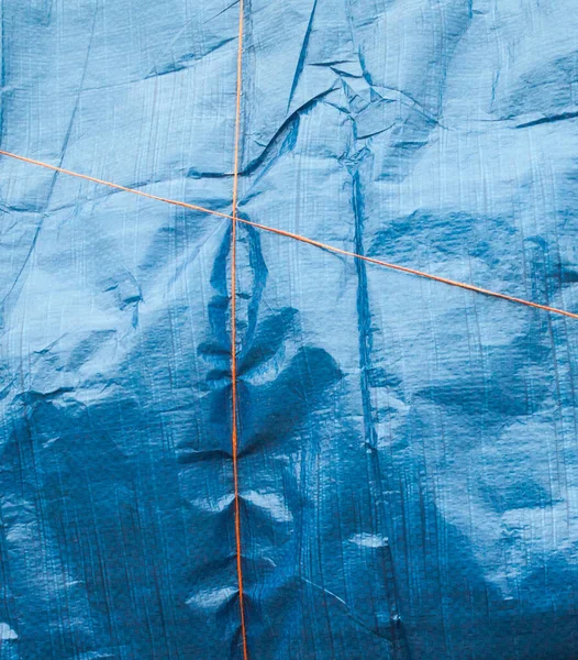 Blue crumpled synthetic fabric tied up with orange thread. Abstract background.
