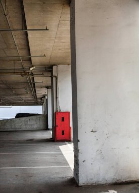 Binanın altına park etmek (otopark altı). Beton kolonlar. Kırmızı yangın güvenlik dolabı.