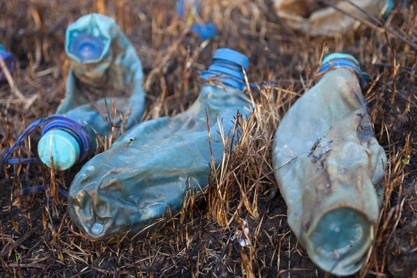 Tres botellas de plástico fundido en la hierba quemada — Foto de Stock