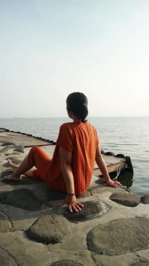 Turuncu gömlekli kadın bulutlu bir günde sakin su sahiline bakan Stoney Rıhtımı 'nda oturuyor, iyileşmek için seyahat ediyor.