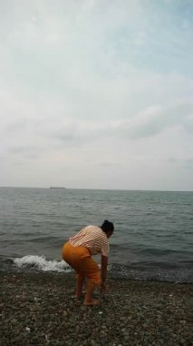 Okyanus esintisini sakin bir plajda kucaklayan Asyalı kadın zihinsel sağlık farkındalığı, tropikal turizm broşürleri ve yaşam tarzı bloglarında kullanmak üzere kişisel iyileşme ve solo seyahat anı yakalıyor.