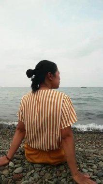 Okyanus esintisini sakin bir plajda kucaklayan Asyalı kadın zihinsel sağlık farkındalığı, tropikal turizm broşürleri ve yaşam tarzı bloglarında kullanmak üzere kişisel iyileşme ve solo seyahat anı yakalıyor.