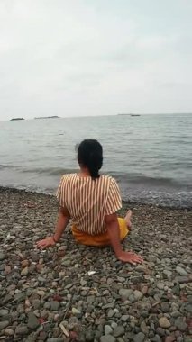 Okyanus esintisini sakin bir plajda kucaklayan Asyalı kadın zihinsel sağlık farkındalığı, tropikal turizm broşürleri ve yaşam tarzı bloglarında kullanmak üzere kişisel iyileşme ve solo seyahat anı yakalıyor.