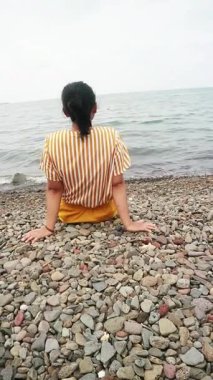 Okyanus esintisini sakin bir plajda kucaklayan Asyalı kadın zihinsel sağlık farkındalığı, tropikal turizm broşürleri ve yaşam tarzı bloglarında kullanmak üzere kişisel iyileşme ve solo seyahat anı yakalıyor.