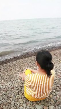 Okyanus esintisini sakin bir plajda kucaklayan Asyalı kadın zihinsel sağlık farkındalığı, tropikal turizm broşürleri ve yaşam tarzı bloglarında kullanmak üzere kişisel iyileşme ve solo seyahat anı yakalıyor.