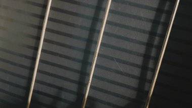 Paslı metal çubuklar, nötr gri bir duvara keskin gölgeler bırakarak endüstriyel markalaşma, kentsel grunge tasarımları ve mimari dokular için çarpıcı geometrik bir arka plan oluşturur.