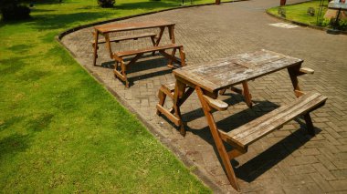 Klasik bir ahşap piknik masası ile bağlı banklar yeşil yemyeşil çimlerle çevrili bir kırsal tuğla veranda üzerinde oturur, arka bahçede yemek, aile toplantıları ve yaz tatili kavramları için davetkar bir açık hava ortamı yaratır.