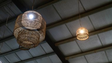 Örülmüş ahşap kolye ışıklarının, birbirine uyumlu koyu dokulu tavana sıcak, rahat bir parıltı saçan, konukseverlik damgası, çevre dostu iç tasarım blogları ve tropikal tatil köyü pazarlaması için mükemmel bir alçak açılı çekimi.