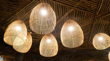 Örülmüş ahşap kolye ışıklarının, birbirine uyumlu koyu dokulu tavana sıcak, rahat bir parıltı saçan, konukseverlik damgası, çevre dostu iç tasarım blogları ve tropikal tatil köyü pazarlaması için mükemmel bir alçak açılı çekimi.