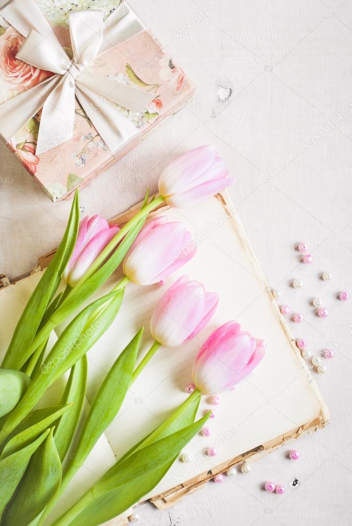 Pink tulips with gift box over white wooden table