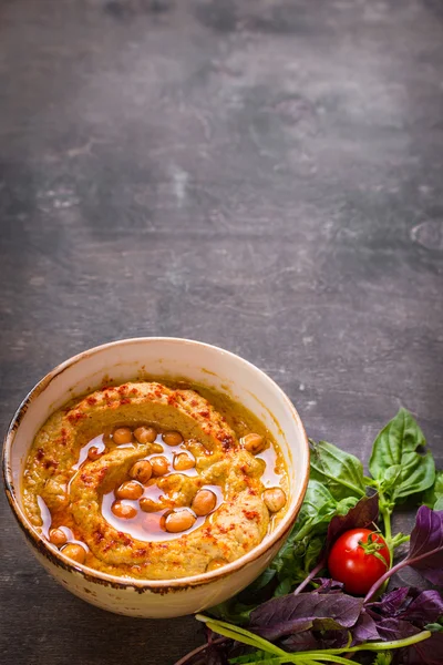 Hummus di piring dengan tomat ceri dan herbal di kayu yang gelap — Stok Foto