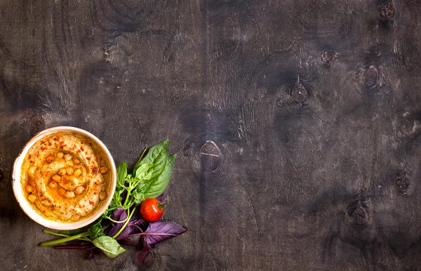 Hummus on a plate with cherry tomatoes and herbs on a dark woode — Stock Photo, Image