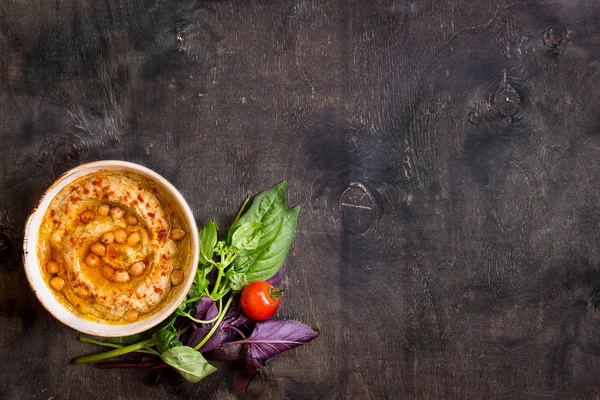 Hummus on a plate with cherry tomatoes and herbs on a dark woode — Stock Photo, Image